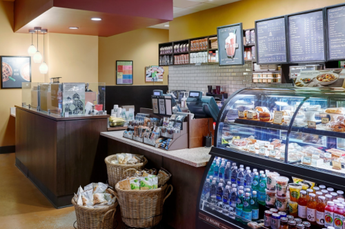 A cozy café interior featuring a service counter, display cases with food, and shelves stocked with products.