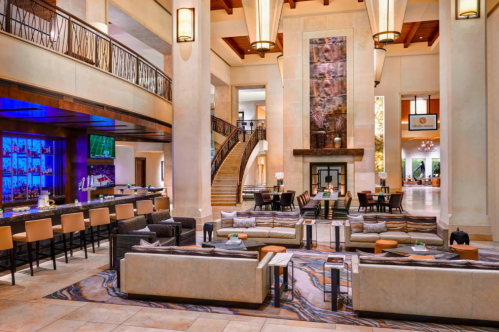 Luxurious hotel lobby with modern seating, a bar area, and a grand staircase, featuring elegant lighting and decor.