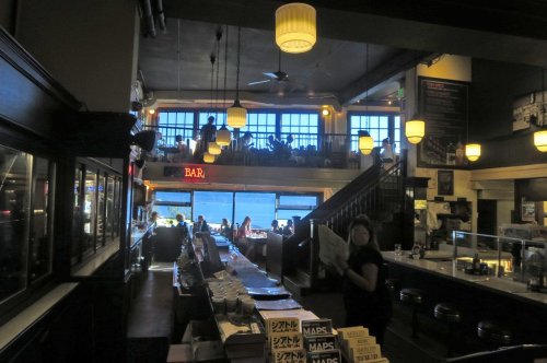 A cozy bar interior with a view of the ocean, featuring tables, a counter, and patrons enjoying the atmosphere.