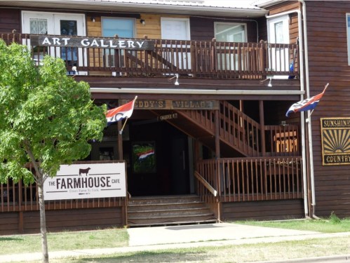 A wooden building with an art gallery sign, a café sign, and flags, featuring a balcony and entrance.