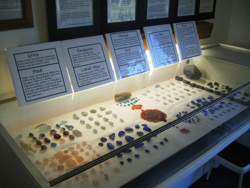 Display case featuring various colored gemstones and minerals, with informational signs above each color category.