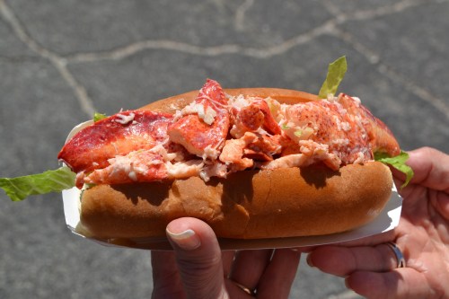 A hand holding a lobster roll filled with lobster meat and lettuce in a soft bun.