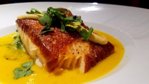 A beautifully plated piece of crispy salmon topped with herbs and a drizzle of sauce on a white dish.