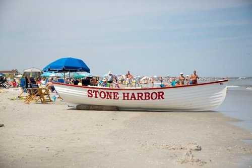 A large white boat labeled "STONE HARBOR" on a sandy beach with umbrellas and people enjoying the sun.