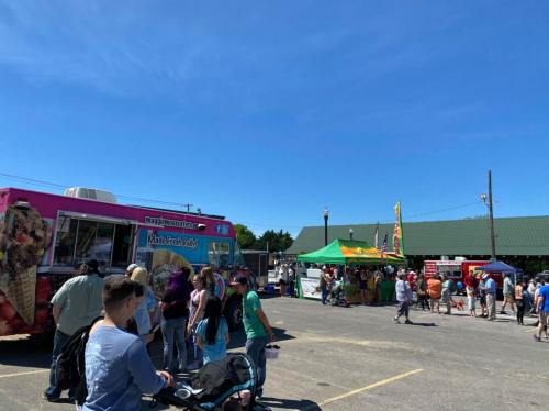 A busy outdoor food truck event with colorful trucks and a crowd enjoying the sunny day.
