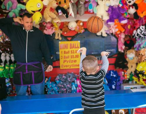A young boy throws a basketball at a game booth filled with stuffed animals and prizes.