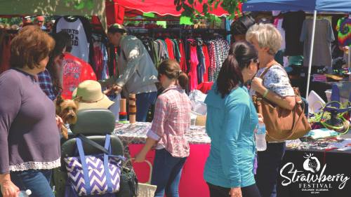 A bustling outdoor market scene with people browsing stalls, colorful tents, and a dog in a stroller.
