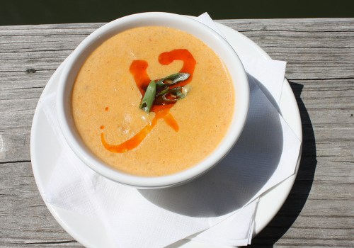 A bowl of creamy soup garnished with green onions and a drizzle of sauce, placed on a wooden surface.