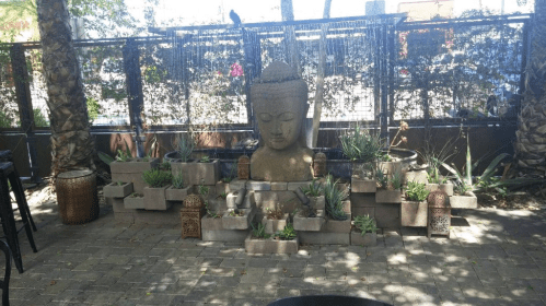 A serene outdoor space featuring a large Buddha statue surrounded by plants and decorative lanterns.