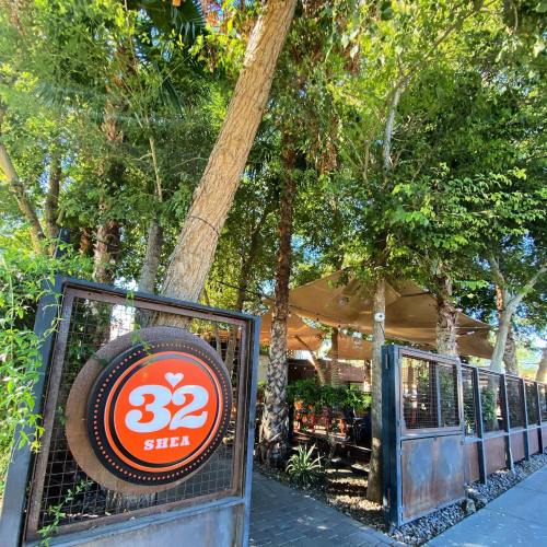 A vibrant outdoor restaurant entrance surrounded by lush greenery and trees, featuring a sign that reads "32 Shea."