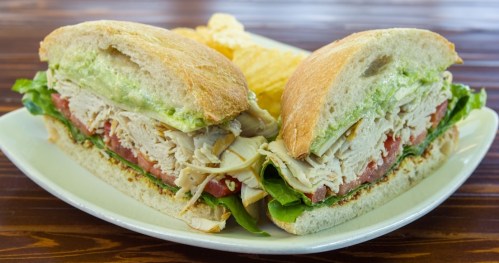 A sandwich filled with turkey, lettuce, and tomato, served with potato chips on a plate.