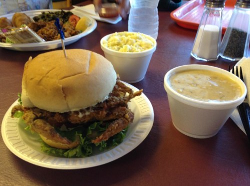 A fried soft-shell crab sandwich on lettuce, served with a side of coleslaw and a cup of clam chowder.