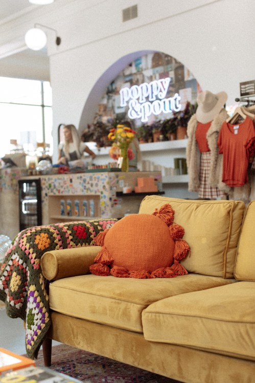 A cozy yellow sofa with a decorative pillow in a stylish shop featuring colorful decor and clothing displays.