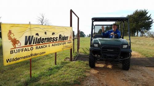 A person waves from a utility vehicle near a sign for Wilderness Rider Buffalo Ranch & Adventure Park.