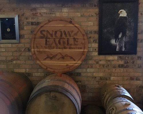 Wooden sign reading "Snow Eagle" on a brick wall, with barrels and a framed eagle photo nearby.