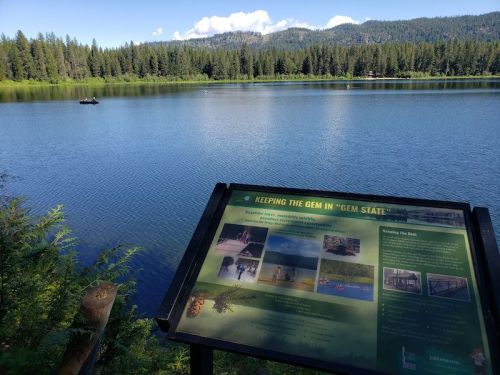 A serene lake surrounded by trees, with a sign about the area's natural features in the foreground.