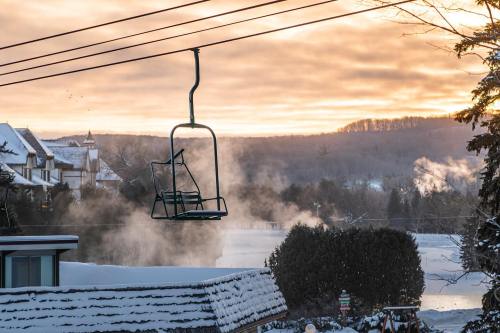 A ski lift chair hangs over a snowy landscape at sunrise, with mist rising from the ground and mountains in the background.