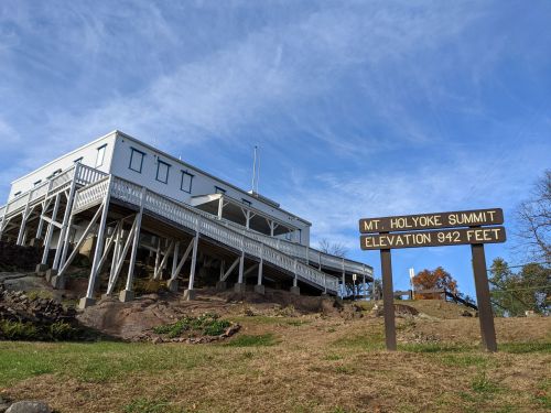 A white building on stilts at Mt. Holyoke Summit, with a sign indicating an elevation of 942 feet.