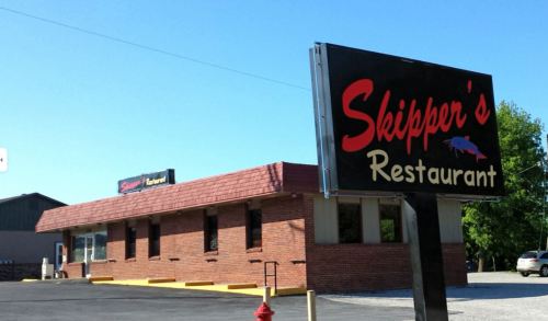 A brick building with a red roof and a sign reading "Skipper's Restaurant" against a clear blue sky.