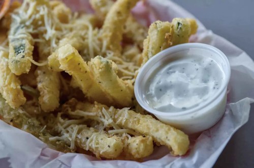 A basket of crispy fried vegetables served with a small cup of creamy dipping sauce.