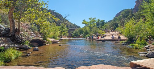 A serene river flows through a lush landscape, with people enjoying the scenery under a clear blue sky.