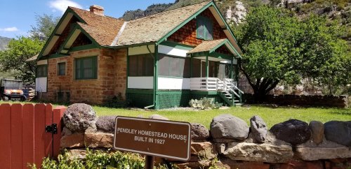 Historic Pendley Homestead House, built in 1927, featuring a green and white exterior and surrounded by greenery.