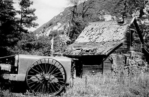 A weathered, abandoned house with a dilapidated roof, next to an old tractor in a rural setting.