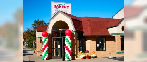 Exterior of Serpe's Bakery with colorful balloon arch, flowers, and a clear blue sky.