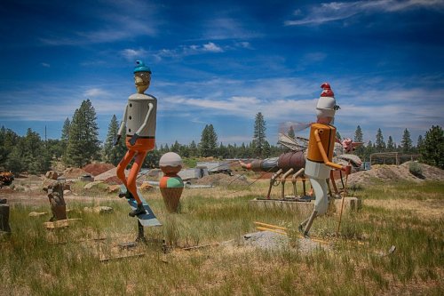 Colorful, oversized sculptures of whimsical characters in a grassy field under a blue sky with scattered clouds.