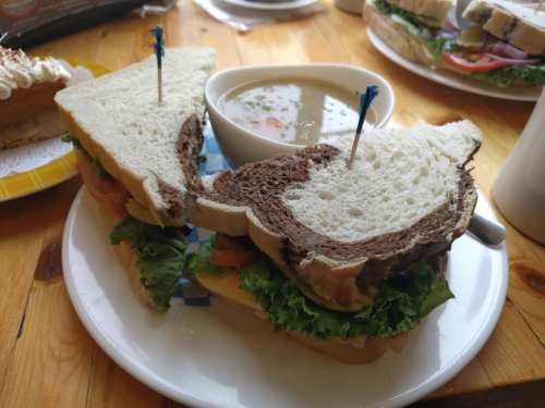 A sandwich with lettuce and tomato on a plate, served with a bowl of soup, featuring two types of bread.