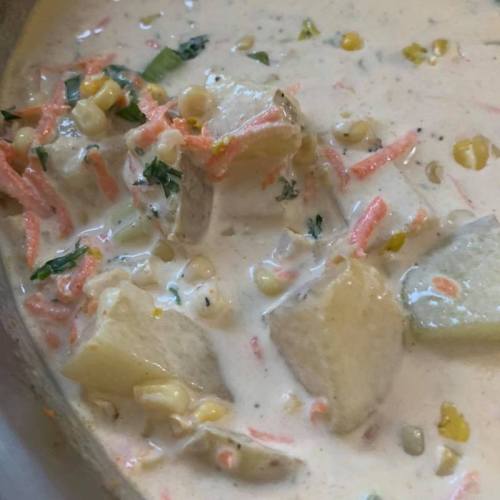 A close-up of a creamy soup with diced vegetables, including carrots and potatoes, in a light-colored broth.