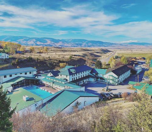 Aerial view of a hotel complex with a pool, surrounded by mountains and open fields under a clear blue sky.