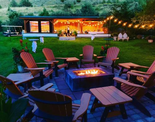 A cozy outdoor space with a fire pit surrounded by chairs, string lights, and a beautifully lit cabin in the background.