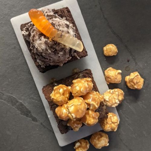 Two brownies topped with popcorn and a gummy worm, served on a slate plate.