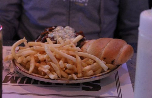 A plate of fries and a sandwich with melted cheese, served on a table.