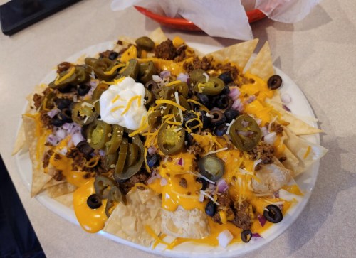 A plate of nachos topped with cheese, jalapeños, olives, onions, ground meat, and a dollop of sour cream.