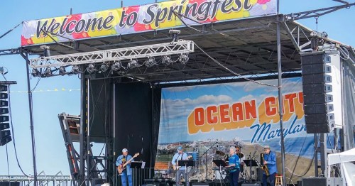 A band performs on stage at Springfest in Ocean City, Maryland, with a colorful banner overhead.