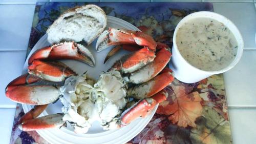 A plate with crab legs, a whole crab, a slice of bread, and a cup of creamy soup on a colorful placemat.