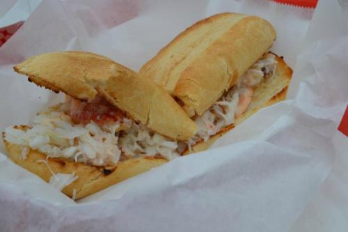 A close-up of a toasted sandwich filled with shrimp, coleslaw, and a tangy sauce, served in white paper.