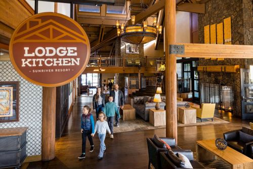 A group of people walks through a spacious lodge interior with wooden beams and a sign for the Lodge Kitchen.
