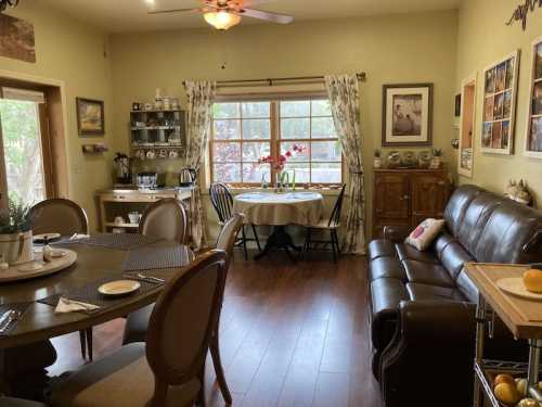 Cozy dining area with a round table, a sofa, and decorative shelves, featuring warm lighting and floral accents.