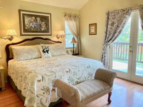 Cozy bedroom with a large bed, decorative pillows, a bench, and doors leading to a balcony, adorned with soft colors.