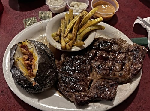 A plate featuring a grilled steak, baked potato with bacon, and a side of golden fries.