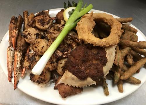 A platter of seafood featuring shrimp, crab, scallops, onion rings, and green beans, garnished with a lemon slice.