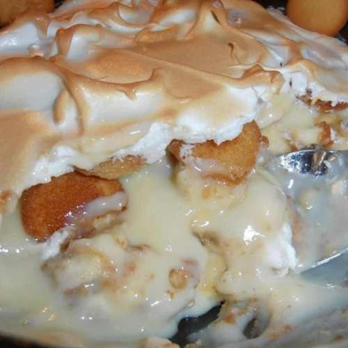 A close-up of a dessert with a golden meringue topping, revealing layers of creamy filling and cake pieces underneath.