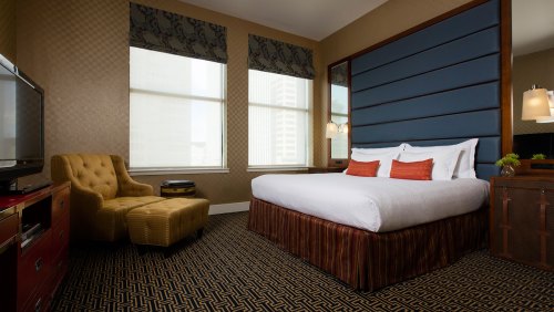 Cozy hotel room featuring a large bed, armchair, and large windows with patterned curtains.