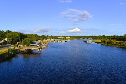 A serene river scene with docks, boats, and lush greenery under a clear blue sky.