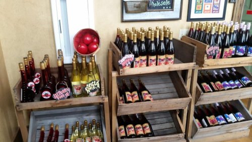 Shelves of various fruit-flavored beverages in wooden crates, with a bowl of red apples on display.