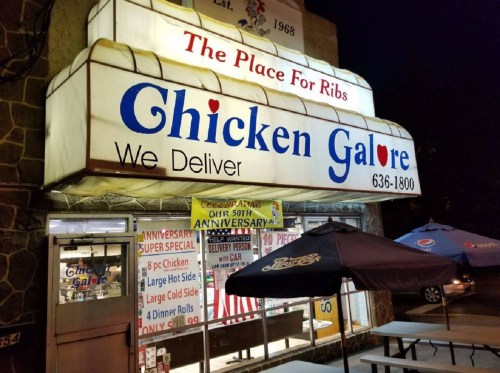 Sign for "Chicken Galore" restaurant, featuring delivery info and anniversary celebration banners outside.