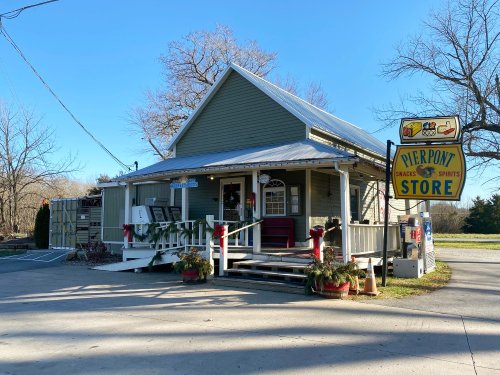 A quaint green store with a porch, festive decorations, and a sign reading "Pierpont Store" in a rural setting.